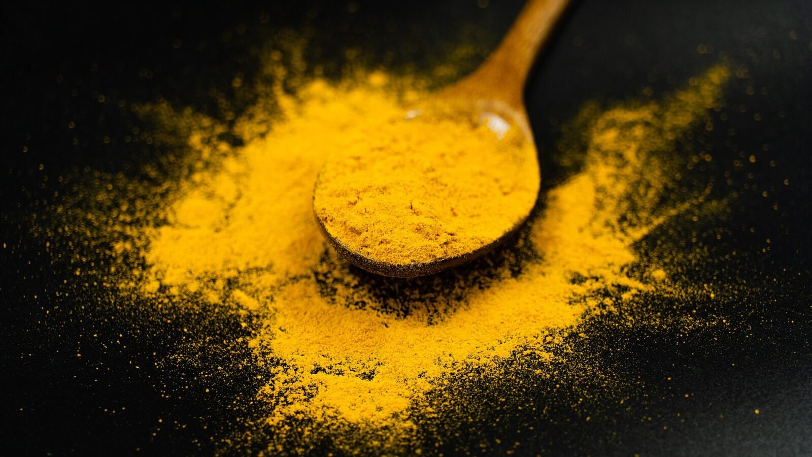Poudre de curcuma jaune vif sur une cuillère en bois, sur fond noir