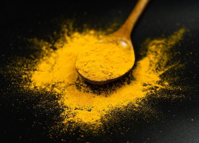 Poudre de curcuma jaune vif sur une cuillère en bois, sur fond noir