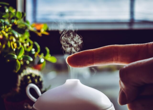 Main effleurant la brume qui s'élève d'un diffuseur ultrasonique devant une fenêtre